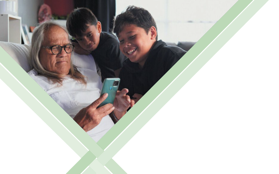 Elderly Māori man looking at a digital device with his grandchildren. 
